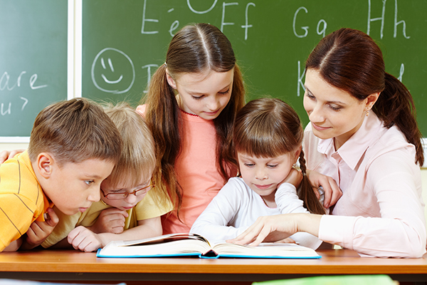 Portrait of smart schoolchildren and their teacher reading book in classroom